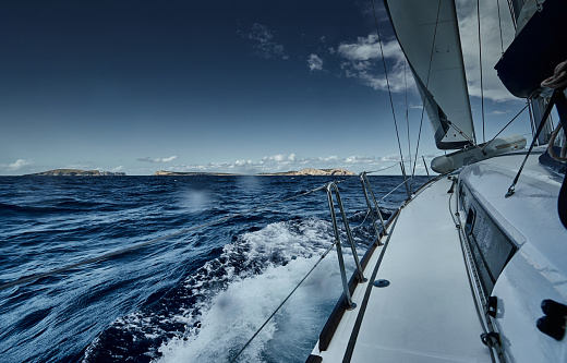 The view of the sea and mountains from the sailboat, edge of a board of the boat, slings and ropes, splashes from under the boat, sunny weather