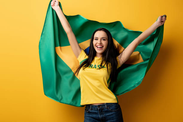 excited female football fan holding brazilian flag on yellow excited female football fan holding brazilian flag on yellow brazil stock pictures, royalty-free photos & images