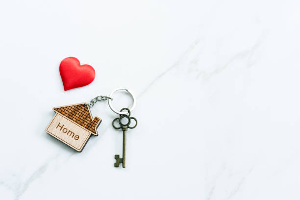 House key with home keyring decorated with mini heart on rusty wood background, copy space stock photo
