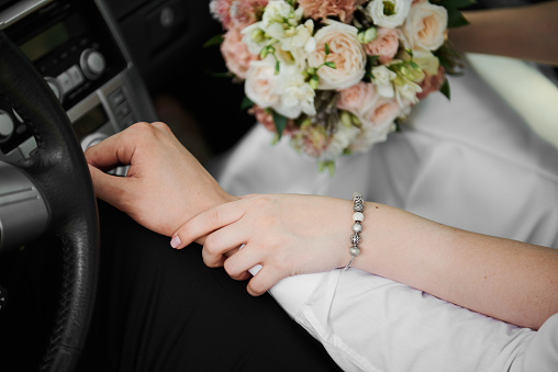 The bride holds the hand of the groom in the car, closeup shot