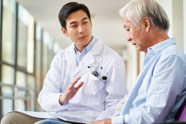 young asian doctor explaining medical condition to senior patient in hospital - doctor asian ethnicity chinese ethnicity young adult imagens e fotografias de stock