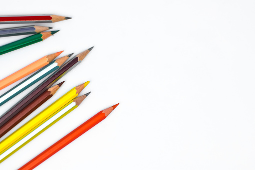 Scattered row of various colored wood pencil crayons arranged together in a line format in front of white background