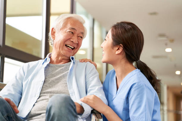 friendly asian caretaker talking to senior patient in nursing home stock photo