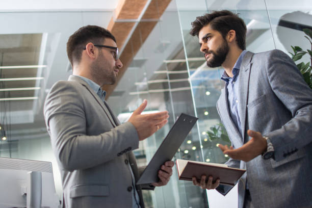 istock Two business men in formal wear discussing contract in modern office 1216391406