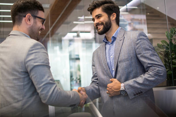 istock Two handsome business partners in formal wear shaking hands in office 1216391409
