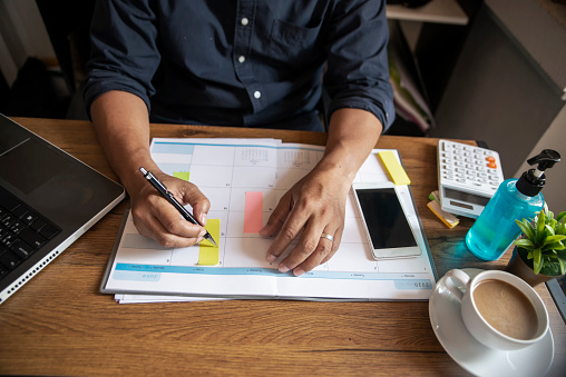 Male hand of planner writing daily appointment On 2020 Calendar book,working space at home.Asian man plan and noted schedule(holiday trip) on the diary at office desk.Calendar for planner concept