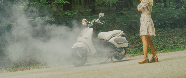 Woman standing near broken down scooter with smoke coming out of it