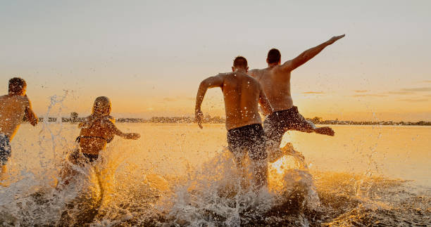 gruppo di amici che corrono e sguazzano nel lago al tramonto - men beach running shirtless foto e immagini stock