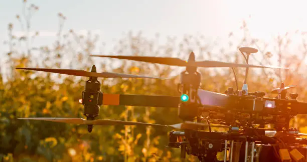 Photo of Photograph with a close-up of a drone in a field during sunset with its propellers visible and plants in the background