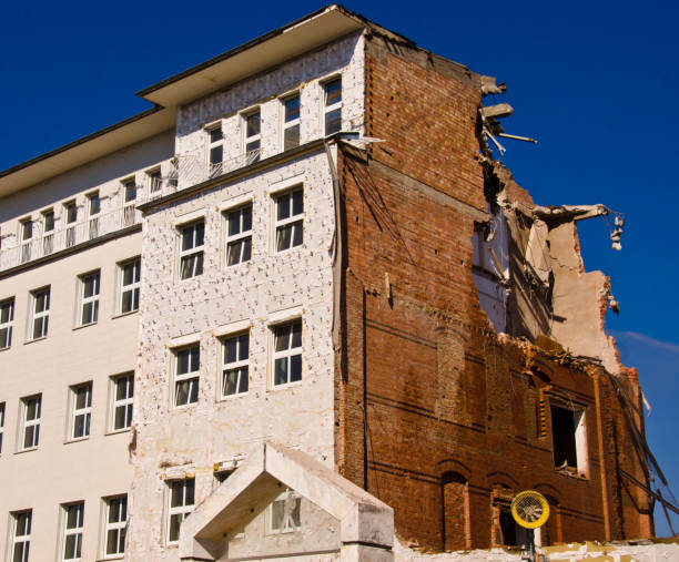 una demolizione di un edificio con una gru con sfondo cielo blu - imploding foto e immagini stock