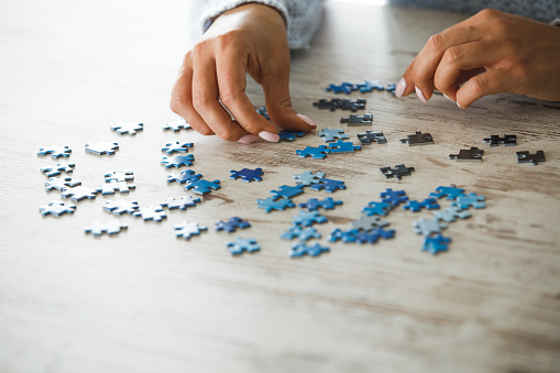 Close up of female hands playing with jigsaw puzzle pieces on wooden table to train concentration, patience and problem solving skills during lockdown time.