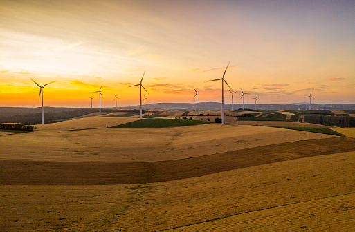 Countryside landscape with an aerial view of patchwork fields and wind turbines under a moody sky at sunset.