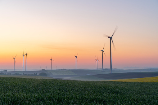 Countryside landscape with view of young green wheat in a field and wind turbines in the background under a moody sky at sunrise