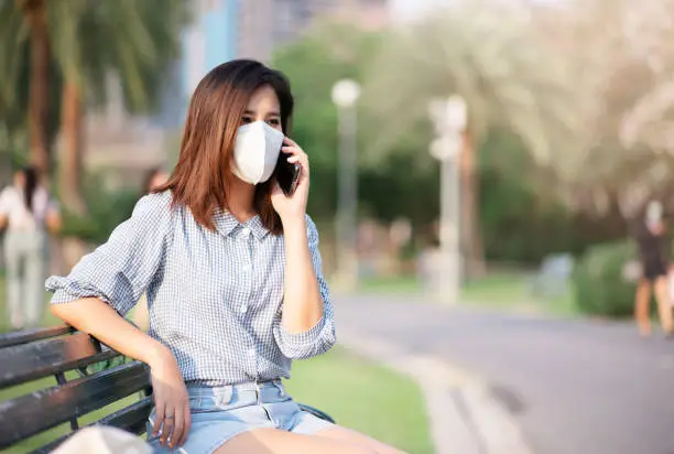 Adult Asian WomanSitting in Public Park. She Wearing Virus Protective Mask in Prevention for Coronavirus or Covid-19 Outbreak Situation - Healthcare and Lifestyle Concept