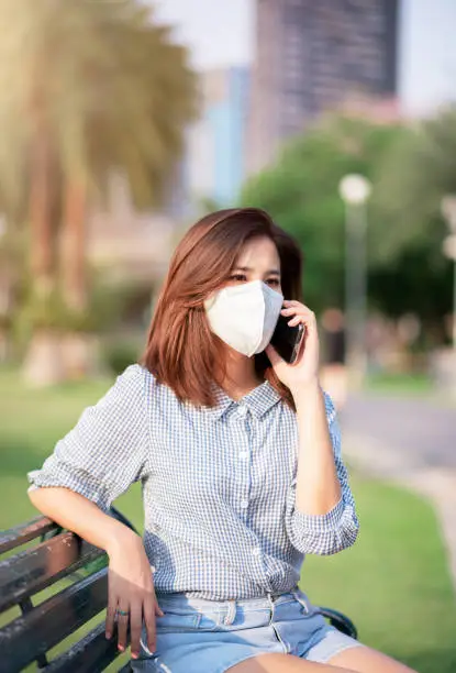 Adult Asian WomanSitting in Public Park. She Wearing Virus Protective Mask in Prevention for Coronavirus or Covid-19 Outbreak Situation - Healthcare and Lifestyle Concept