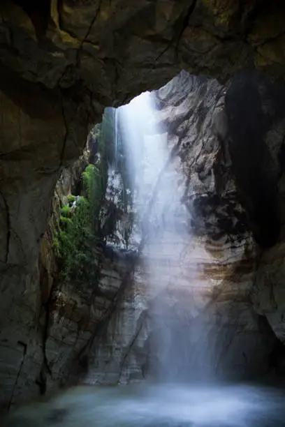Photo of Light shining through waterfall in a an ancient cave