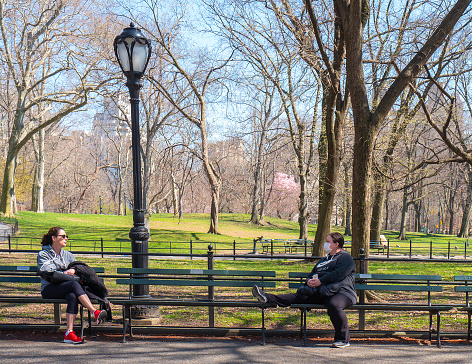 Manhattan, New York, USA - March 26, 2020:  New Yorkers Social distancing in Central Park, wearing surgical mask to help prevent the spread of Covid-19 coronavirus.