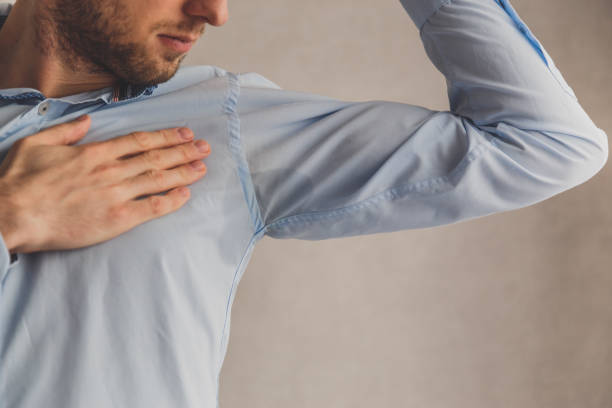 Man with hyperhidrosis sweating very badly under armpit in blue shirt, on grey. Man with hyperhidrosis sweating very badly under armpit in blue shirt, on grey body odor stock pictures, royalty-free photos & images