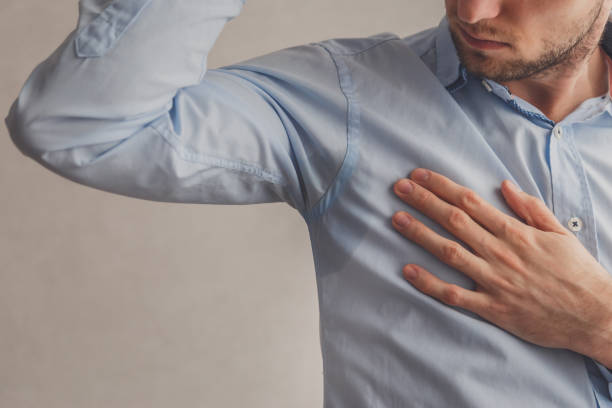 istock Man with hyperhidrosis sweating very badly under armpit in blue shirt, on grey. 1216415802