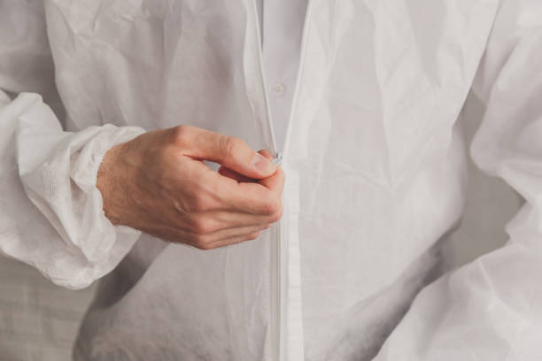 istock Doctor epidemiologist puts on white protective overalls, fastens a zipper, hands close-up. Hands in protective rubber gloves. Personal protective equipment concept. 1216415809