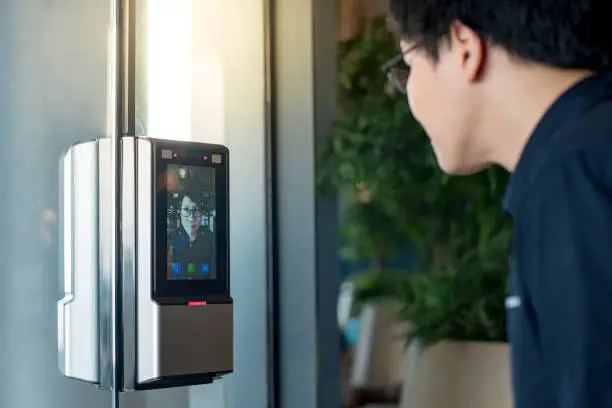 Authentication by facial recognition concept. Biometric admittance control device for security system. Asian man using face scanner to unlock glass door in office building.