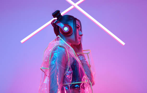 Elegant beautiful asian woman in a fashionable raincoat listens music Portrait of elegant beautiful asian woman in a fashionable raincoat listens music in headphones around colourful bright neon uv lights posing in studio raincoat photos stock pictures, royalty-free photos & images