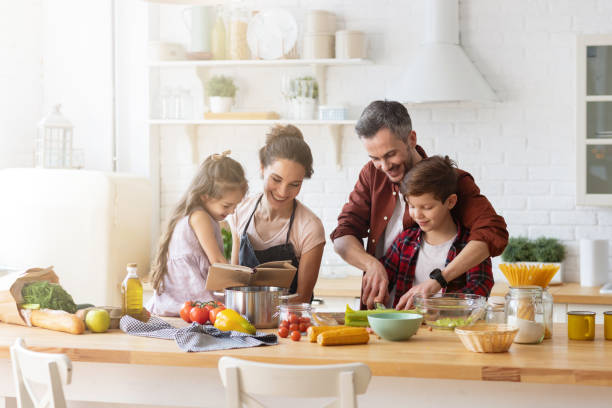 Happy family cooking together on home kitchen Happy family cooking together on kitchen. Mother and daughter reading recipe to father and son. Dad and boy chopping green vegetable leaf for salad. Home recreation and food preparation on weekend cooking stock pictures, royalty-free photos & images