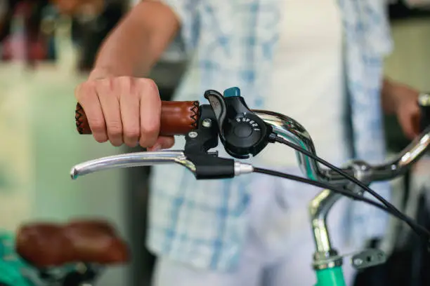 Cut out of metalic steering wheel, leather handle bar and brake lever of a bicycle held by female hand. Gear shifter offers six possibilities.