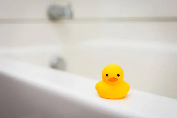 Miniature baby rubber duck on the ledge of white bath tub