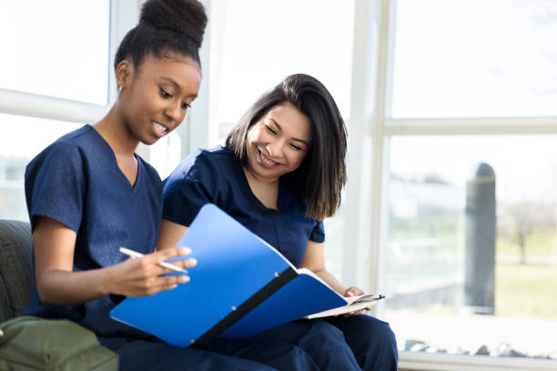 Young adult female nursing students study together The two young adult female nursing students sit next to each other to study. They are sharing notes. community college stock pictures, royalty-free photos & images