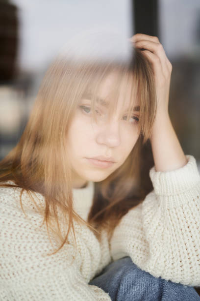 istock Young girl looking to window feeling sorrowful and unhappy 1216426820
