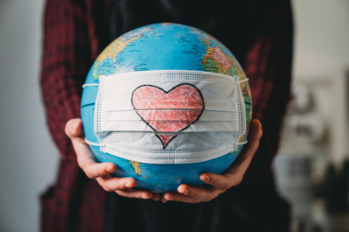 Young woman holding a globe with a face mask on it - Conceptual Coronavirus Covid-19 virus pandemic - Heart shape is drawn on the mask.