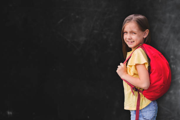 istock cute little girl   standing against blackboard copy space 1216427993