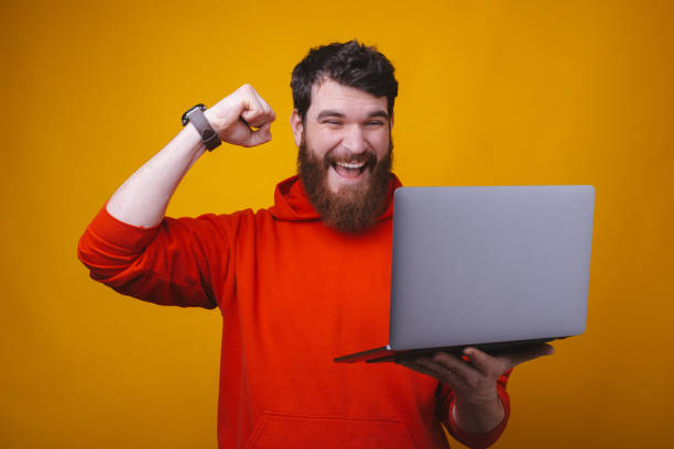 istock I won. A young bearded man is showing the winner gesture while looking at his laptop he holds. 1216428546