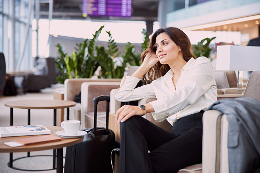 Smiling young woman sitting in comfortable chair in departure lounge stock photo