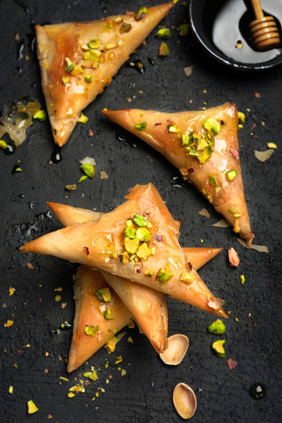 istock Arabe phyllo sweets. Feta cheese Phyllo Triangles pies with honey and pistachios, selective focus. Cooking sweets turkish, or arabic traditional ramadan pastry dessert on a dark background. Top view. 1216429330