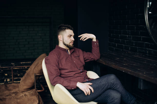 A young man sits on a chair in his room