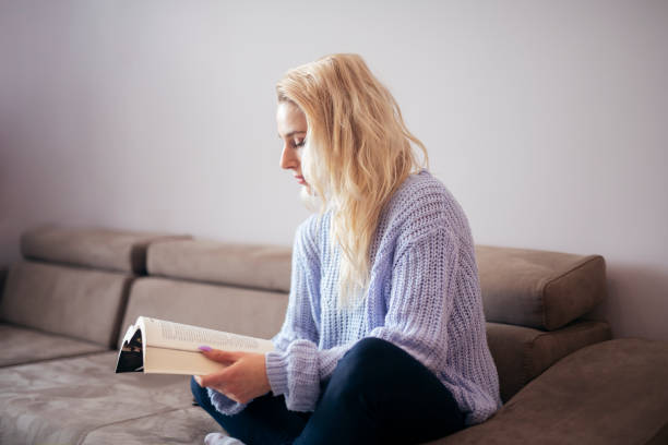 Woman sitting on sofa and reading book at home.
