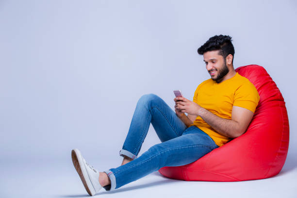 hombres jóvenes relajándose en la silla de bolsa de frijoles sobre fondo blanco foto de stock - one floor fotografías e imágenes de stock