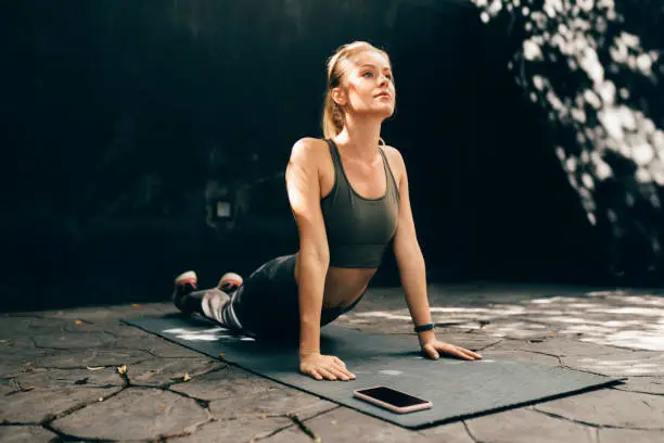 Exercising With a Fitness App: Fit Blonde Woman Doing Yoga Outdoors