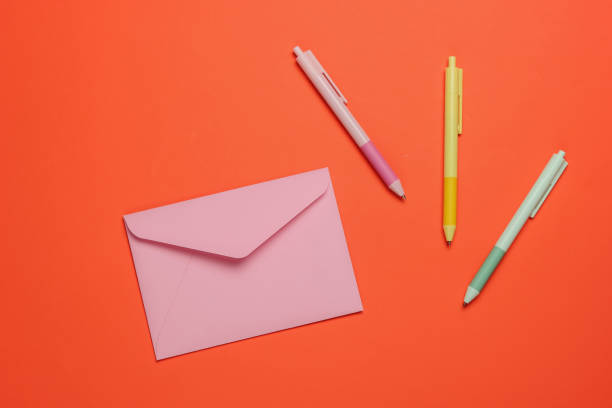 istock Envelope and colored pens on orange background. Top view 1216436425