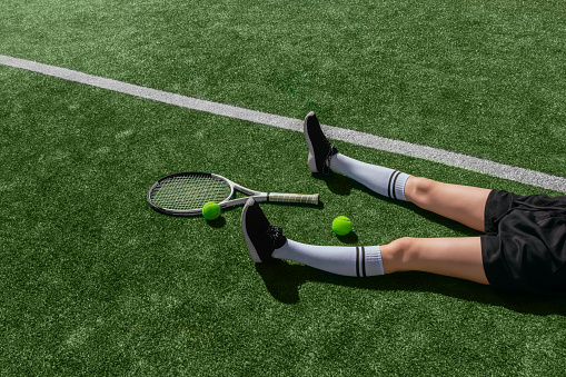 Girl in black sportswear is lying on playing field with a tennis ball and a racket