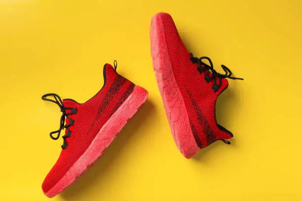 Red sports shoes on yellow background, top view.