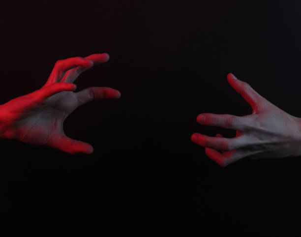 istock Two hands are drawn to each other on a black background with red neon light. Halloween concept 1216439568