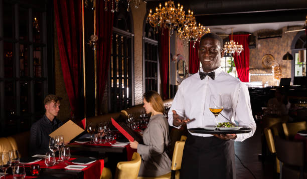 istock Polite waiter holding tray in restaurant with customers behind him 1216441123