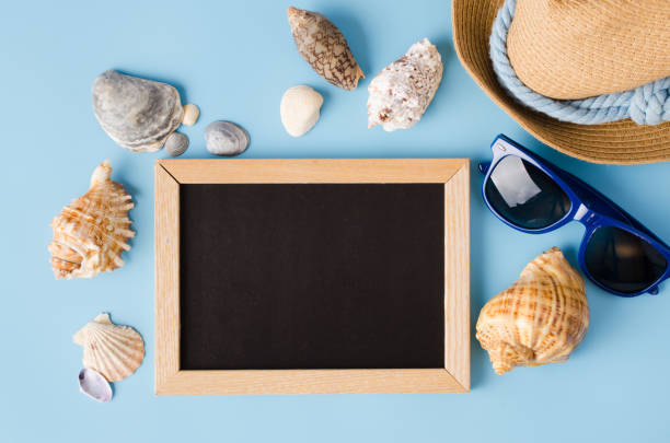 istock Empty chalkboard with seashells, hat and glasses on blue background. 1216442574