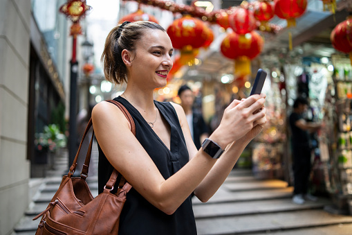 Blond woman browsing on smart phone on street with red lanterns.