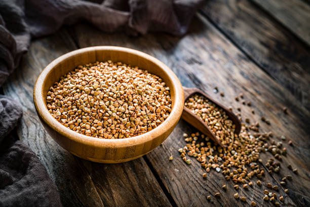 Dietary fiber: high angle view of wholegrain buckwheat in a wooden bowl on rustic kitchen table. A wooden serving scoop with buckwheat is beside the bowl. The composition is at the left of an horizontal frame leaving useful copy space for text and/or logo at the right. Predominant color is brown. XXXL 42Mp studio photo taken with SONY A7rII and Zeiss Batis 40mm F2.0 CF