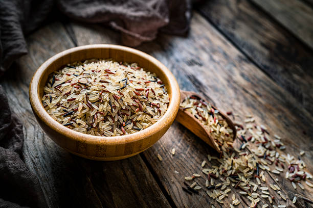 cuenco de madera relleno con arroz mezclado rodado en la mesa de cocina rústica - brown rice fotos fotografías e imágenes de stock