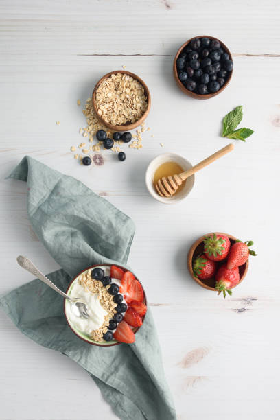 tazón de yogur con bayas y avena sobre la mesa - spoon napkin silverware white fotografías e imágenes de stock